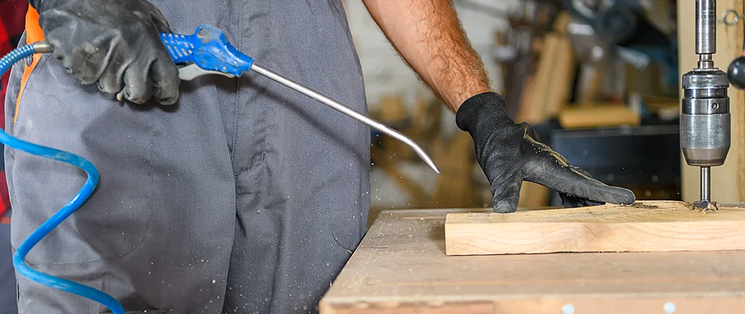 Ein Mann in einer Werkstatt nutzt Pneumatik, um mit einem Druckluftwerkzeug Späne zu beseitigen